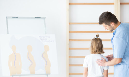 Male physiotherapist examining girl with scoliosis during rehabilitation