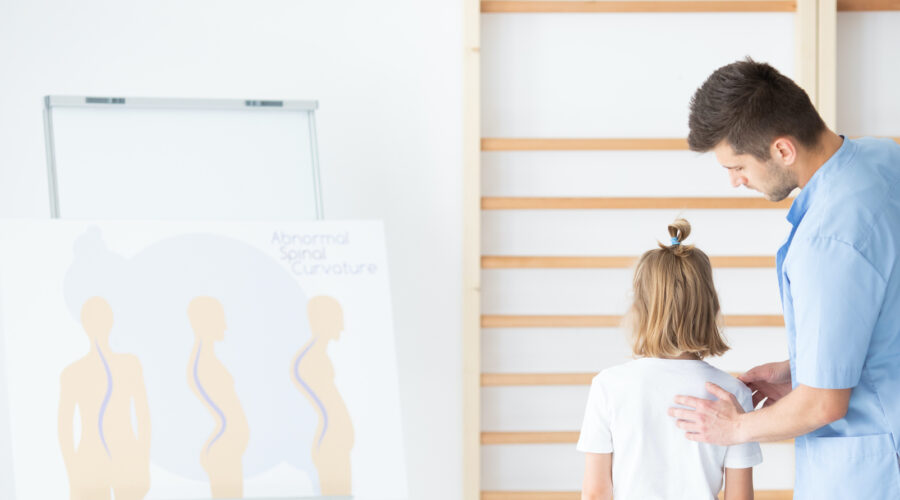 Male physiotherapist examining girl with scoliosis during rehabilitation